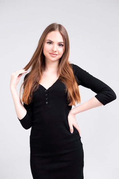 Model with a slim figure posing in a black dress dress girl with long hair on a light background Modeling