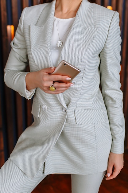 A model woman in a business suit with a phone in her hands. Clothing demonstration in a showroom