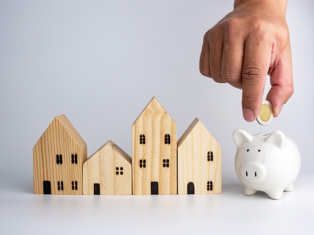 A model wooden house and a man's hand holding a coin. Housing business concept.