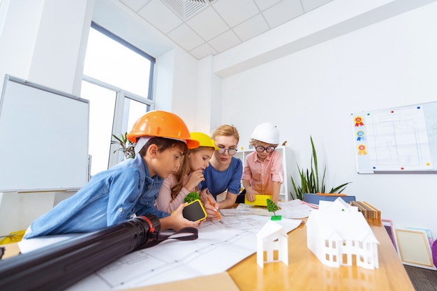 Modeling smart city. Children wearing bright helmets constructing and modeling smart city with teacher