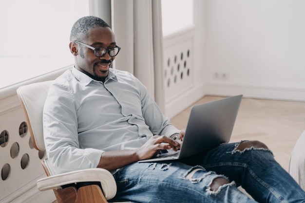 Modern african american businessman in glasses working typing on laptop sitting in office chair