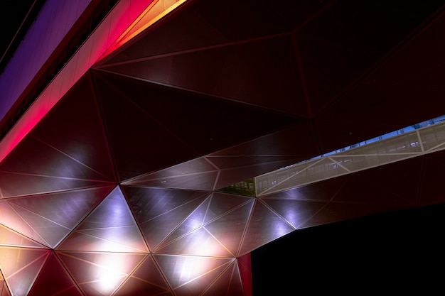 Modern architecture. Orange and red geometric metallic construction from triangular parts. Abstract background design in the dark.