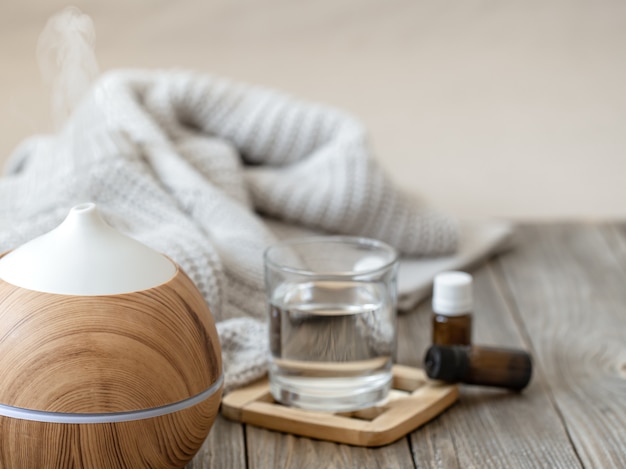 Modern aroma oil diffuser on wood surface with knitted element, water and oils in jars.