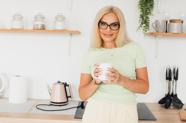 Modern attractive middle-aged woman drinking coffee in the kitchen at home