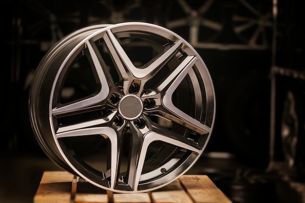 Modern automotive alloy wheel made of aluminum on a black background, industry. on a textured wooden table.