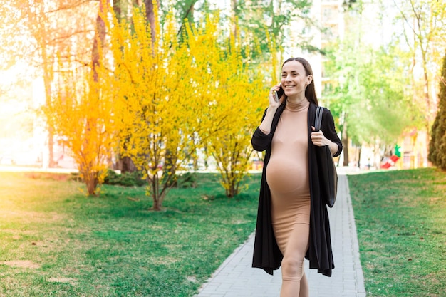 Modern Beautiful Pregnant Walking on City Park with Smart Phone Pregnant Outdoors