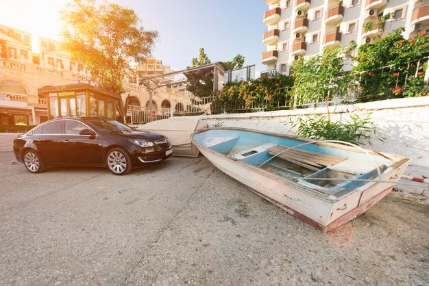 Modern black car and an old wooden boat on a city street