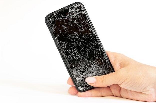 Modern black smartphone with highly broken screen in women hand on white wall