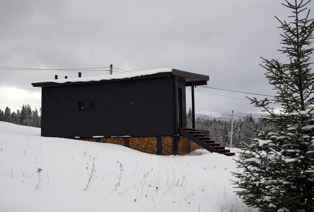 Modern Black wooden cabin in pine forest in snowy weather