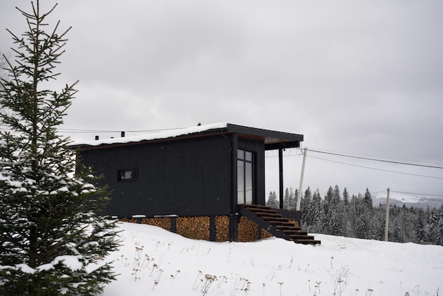 Modern Black wooden tiny cabin in snowy pine forest