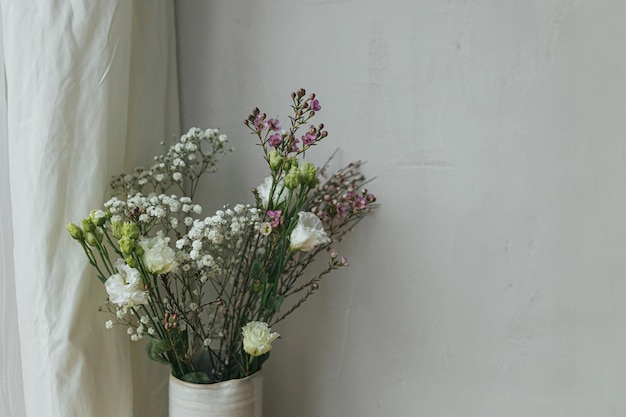 Modern bouquet in vase against tulle and rustic wall Stylish spring flowers eustoma gypsophila and chamelaucium Floral greetings space for text Happy women's day and mother's day