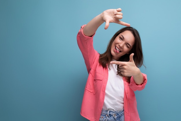 Modern brunette woman in pink shirt makes photo using phone on studio background