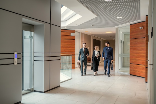 Modern business colleagues of different ages walking in corridor and discussing plan of work day