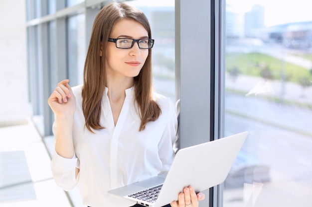 Modern business woman typing on laptop computer while standing in the office before meeting or presentation