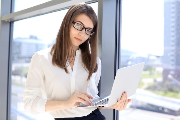 Modern business woman typing on laptop computer while standing in the office before meeting or presentation