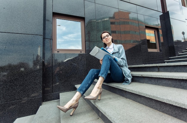 Modern business woman with a folder of documents sits on the stairs Lifestyle