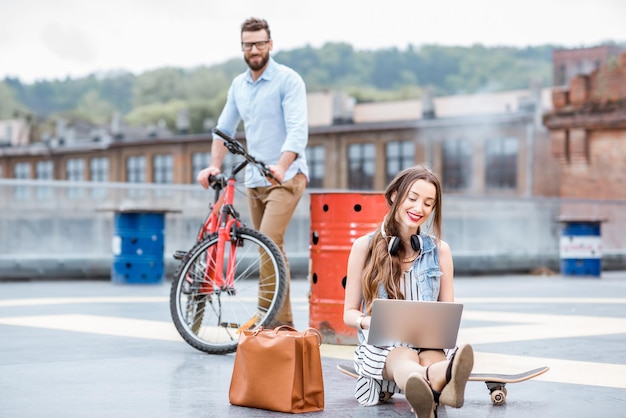 Modern businessman and businesswoman with laptop and bicycle outdoors on the playground. Lifestyle business concept