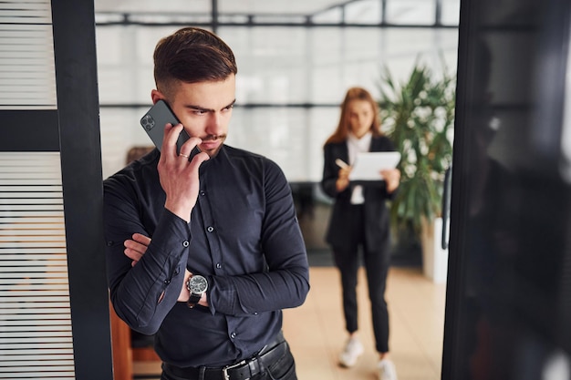 Modern businessman standing indoors in office. His female colleague behind.