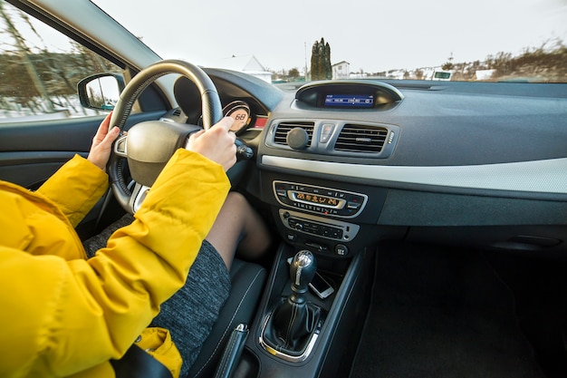 Modern car interior with driver female hands on steering wheel, winter snowy landscape outside. Safe driving concept.