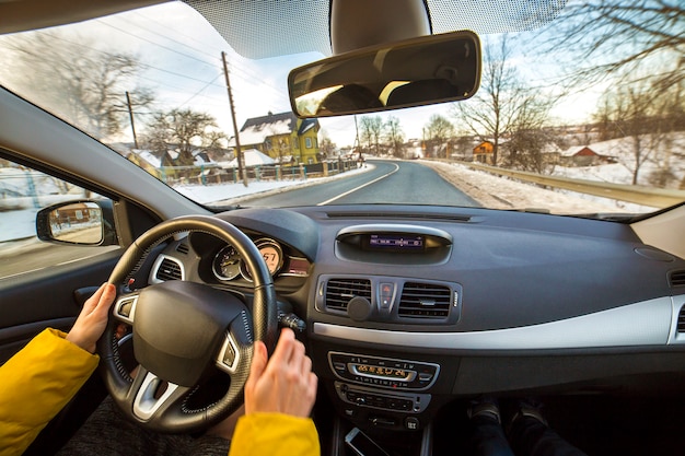 Modern car interior with driver female hands on steering wheel, winter snowy landscape outside. Safe driving concept.