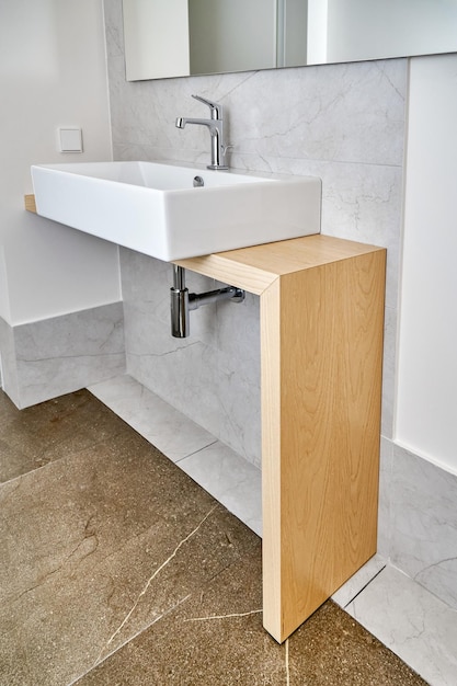 Modern ceramic sink with faucet installed on wooden console table in bathroom