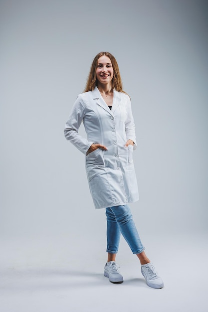 Modern cheerful doctor in a white coat on a gray background Woman doctor with a smile on her face