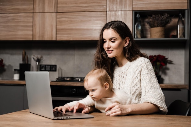 Modern childhood Mom is sitting with toddler child and working on laptop remotely Maternity leave for young mother Happy family time with daughter at home