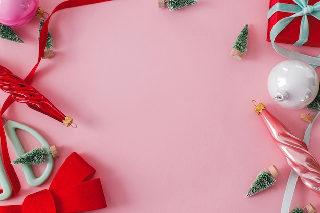 Modern Christmas pink flat lay Stylish red bow baubles little trees and ribbons on pink paper