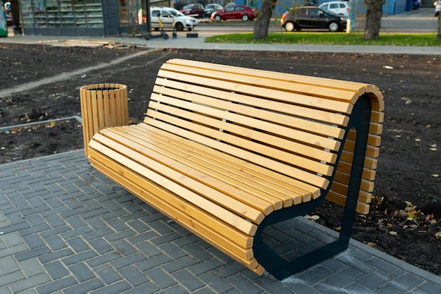 A modern comfortable wooden bench with a backrest and a garbage can made of wooden slats in a new residential area. Landscaping of the house territory