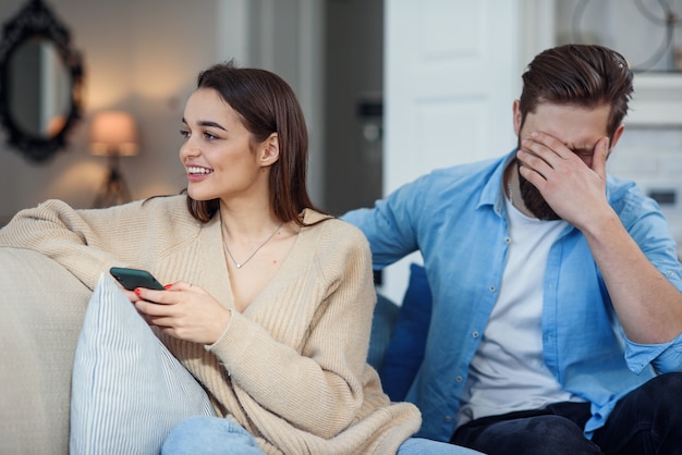 Modern couple at home. Man and woman concentrated on messaging with smartphones, ignoring each other and spending time on social media.