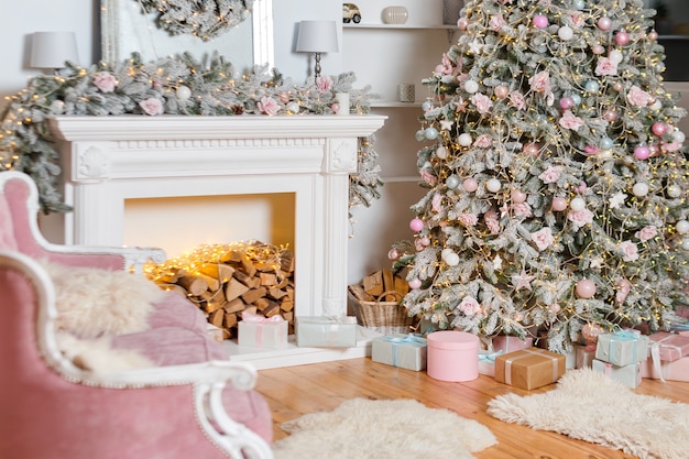 Modern design of the room with fireplace in light colors decorated with Christmas tree and decorative elements, New Year decorations, Happy Winter Holidays, Christmas tree and presents.