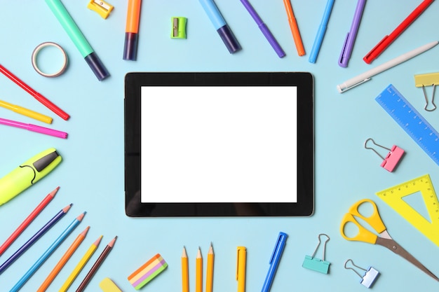 Modern digital tablet and school stationery on a colored background top view