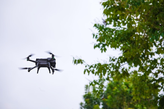 Modern drone flies in the forest Dark drone in the air against