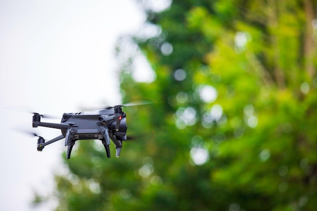 Modern drone flies in the forest Dark drone in the air against