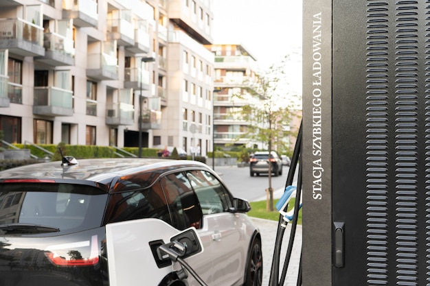 A modern electric car connected by a cable to a power supply unit charges the batteries at a city fast charging station