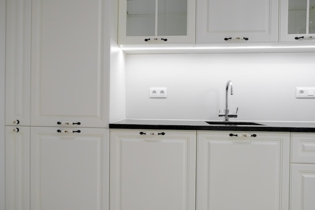 Modern and elegant kitchen with white drawers and cupboards black marble countertop and builtin sink with silver tap