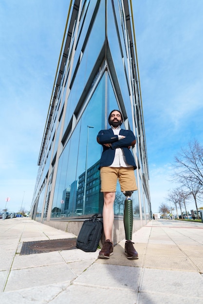 Modern executive with prosthetic limb standing tall crossed arms in front of a towering urban glass