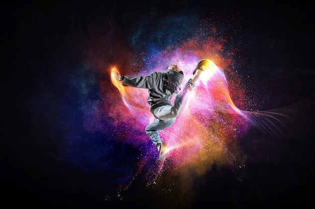 Modern female dancer in hoodie in action with colourful splashes background. Mixed media