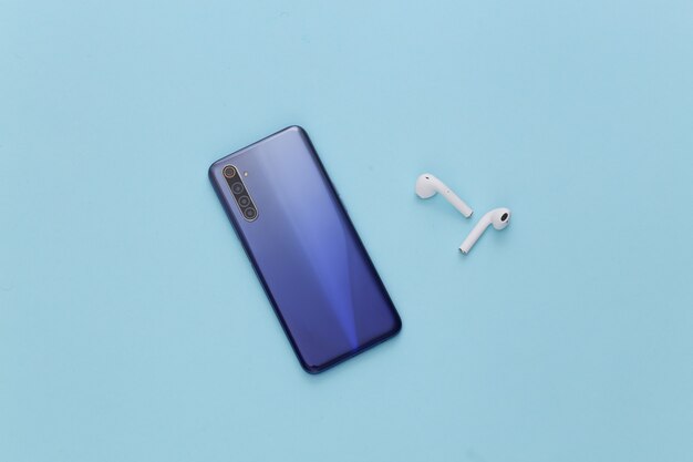 Modern gadgets. Modern smartphone with wireless earphones on blue