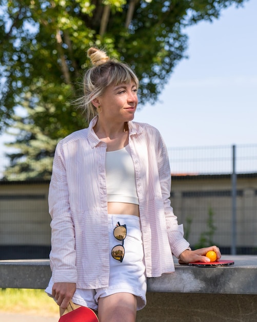 modern girl in short shorts stands near the tennis table holds rackets in her hands