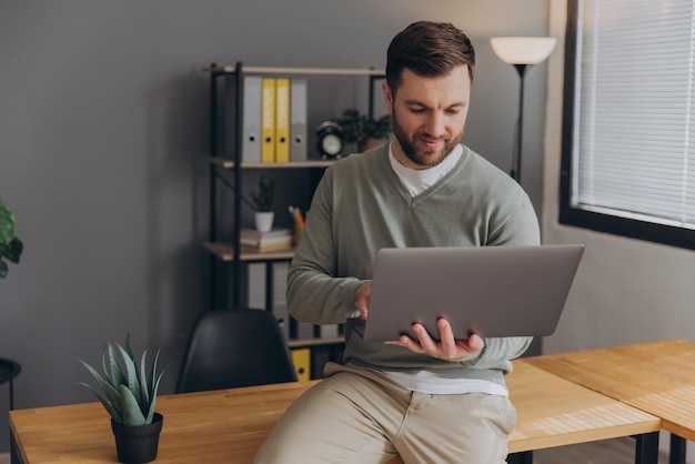 Modern happy bearded office male worker of IT company smiling and holding laptop in office