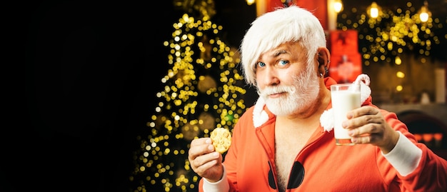 Modern hipster senior santa enjoying in served gingerbread cake and milk funny santa holding glass w