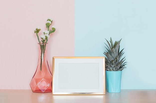 Modern home decor with gold mock up photo frame, vase and tropical plant on pink blue back