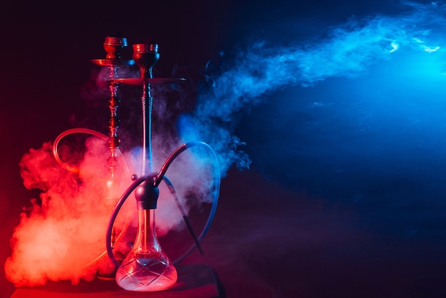 Modern hookah, shisha on a smoky black background with neon lighting and smoke.