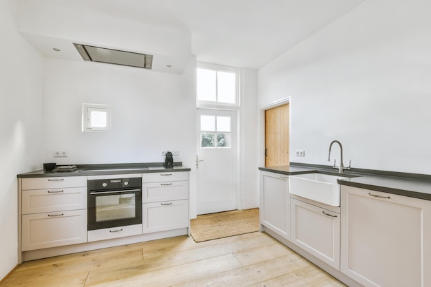 Modern interior design at white contemporary kitchen in loft style, Wooden white cabinet with built in household appliance, electric stove, oven, sink on worktop and extractor hood on white wall