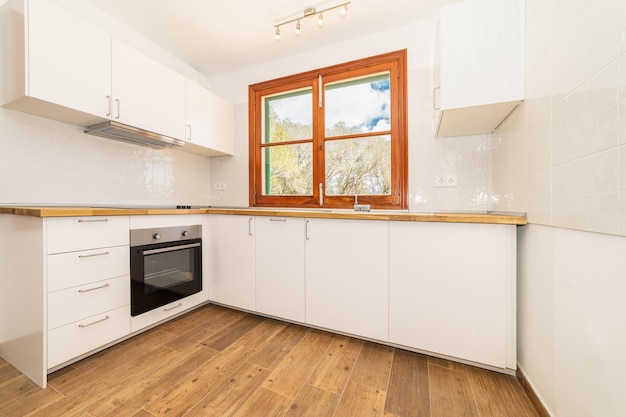 Modern kitchen in a country house with a window, white walls, tiles and wooden floor