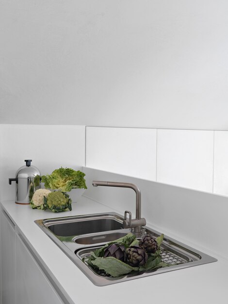 Photo modern kitchen interior in the foregorund the integrated steel sink with some vegetables on the worktop