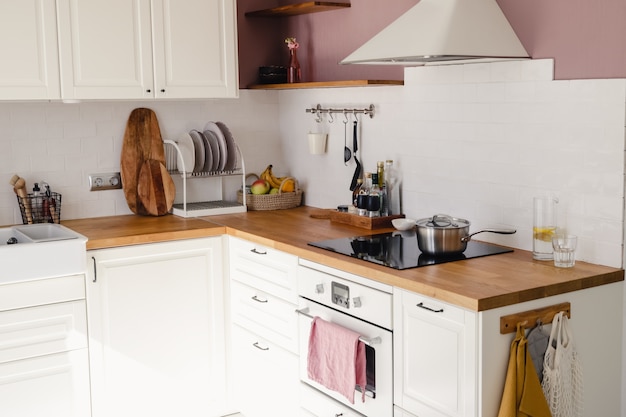 Modern kitchen with white cabinets, wood counter and dining table in sunlight in daytime. Full set of kitchen equipment.