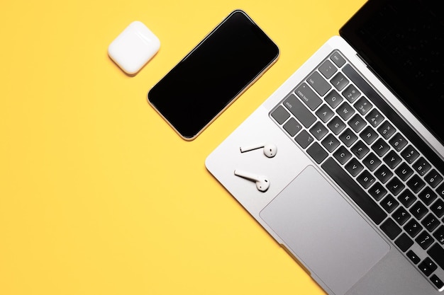 Modern layout of a smartphone with touch screen grey laptop with a black keyboard wireless earphones