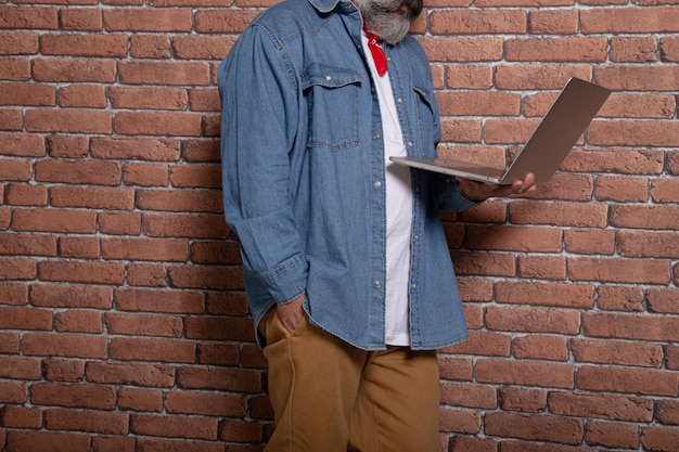 Modern man leaning on the brick wall holds a laptop. Coworking space